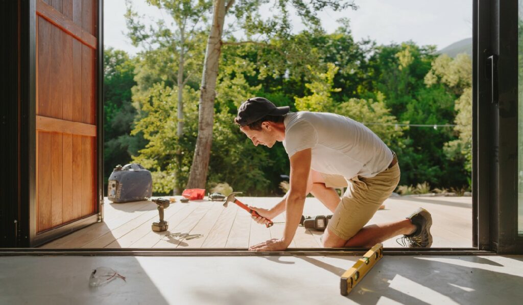 Photo of a carpenter installing wooden decking in front of a cabin house