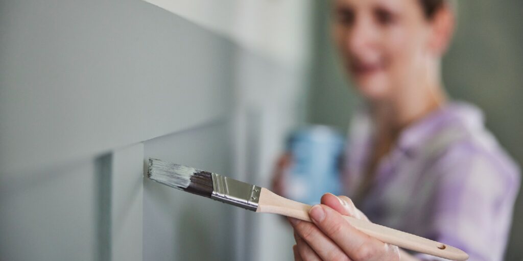 Woman Painting Wall With Panelling In Room Of House With Paint Brush