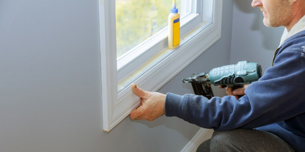 Carpenter close up using on air nail gun to moldings for window