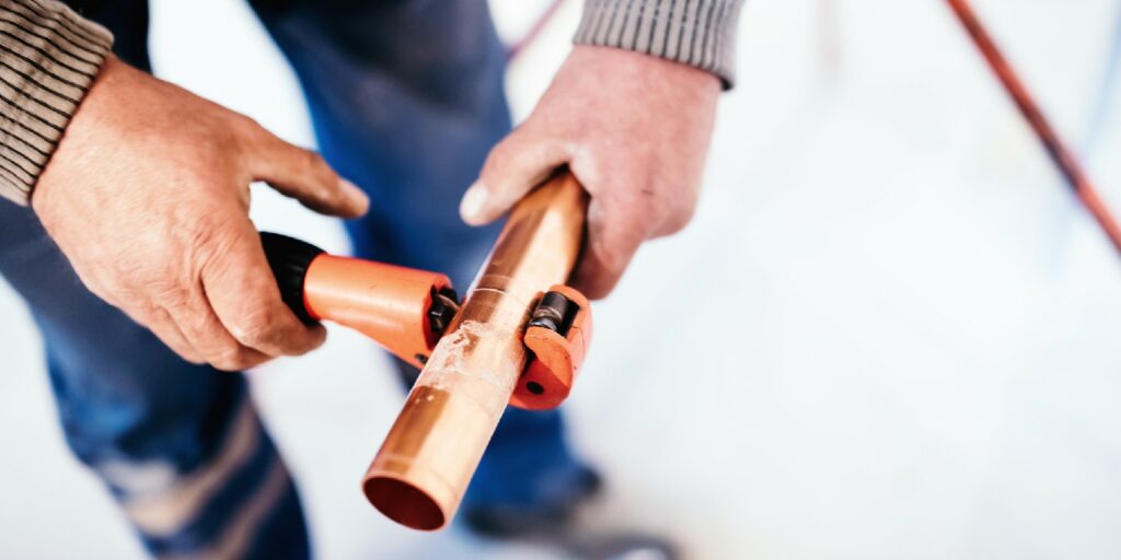 Industrial Plumber cutting a copper pipe with a pipe cutter.