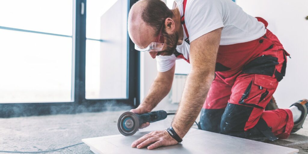 Side view image of tile mason cutting big ceramic tile with electric grinder