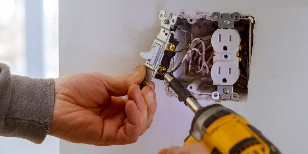 The hands of an electrician installing a power switch to the electrical junction box