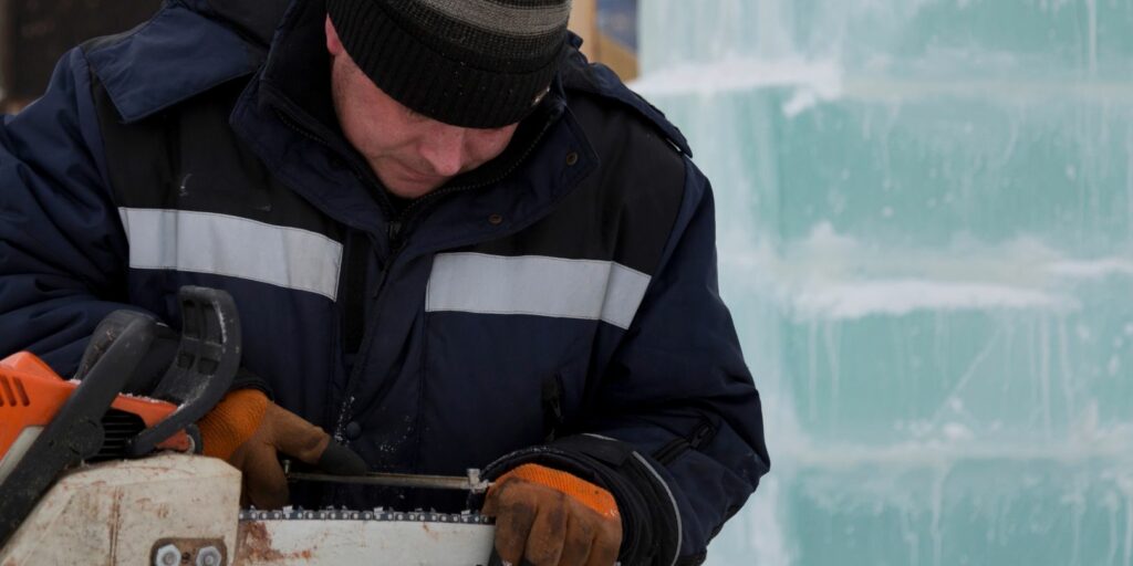 A worker in a blue jacket sharpens a chainsaw chain.