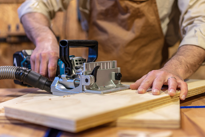 A man using a wood jointer on a plank of wood.